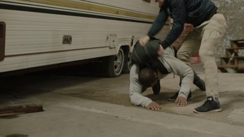 Enraged man fights and tussles with an aggressive man wearing a black backpack, in front of a camper trailer in moody lighting. Medium shot in 4K with an Alexa Mini camera