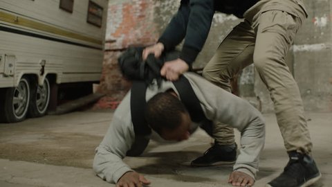 Angry blonde caucasian man fights and tussles with an African American man wearing a black backpack, in front of a camper trailer in moody lighting. Medium shot in 4K with an Alexa Mini camera