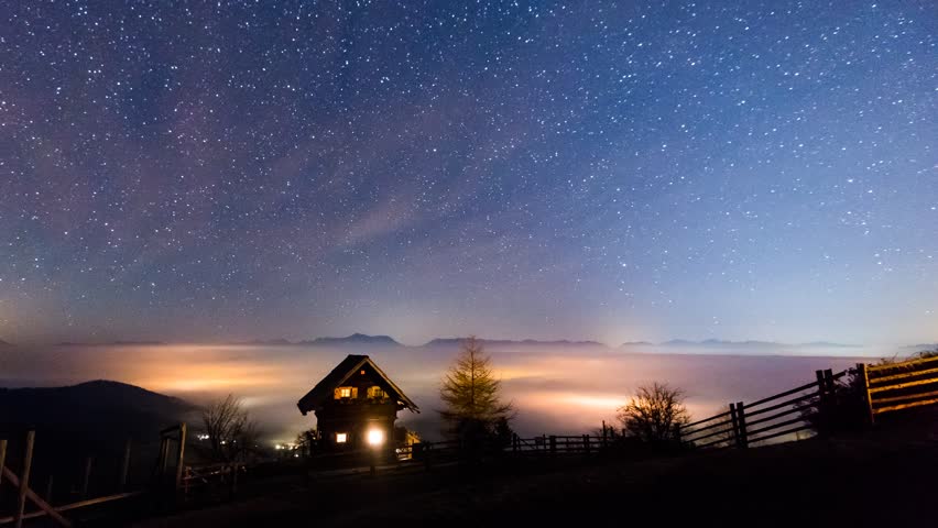 Time Lapse - Traditional alpine cabin at night with rising fog around the house
