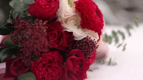 Wedding bouquet of red and white flowers on snow in evergreen conferous woods. Close and macro view of tender roses on snowy surface during snowfall in spruce winter forest.
