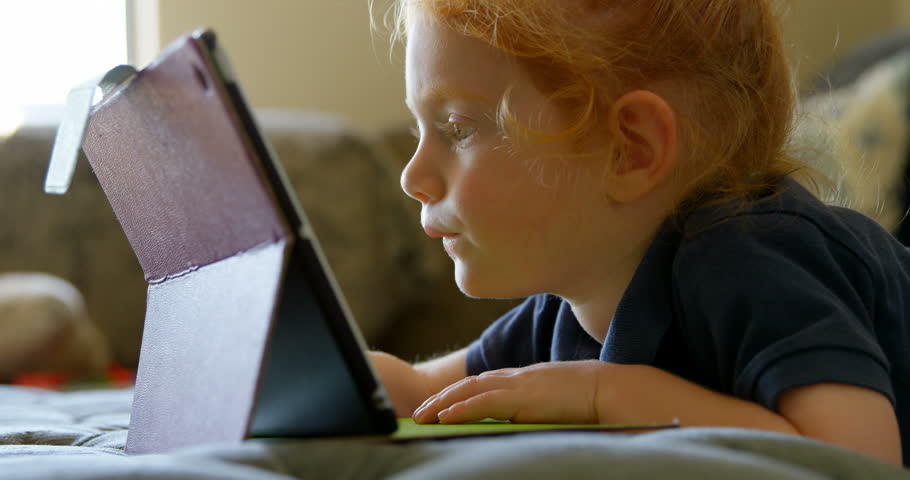 Side view close up of a cute little girl using digital tablet in living room at home. 