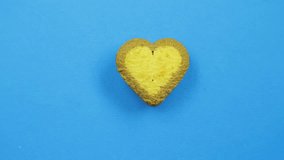 A female hand draws funny faces on a blue background with a brown icing from a tube on a heart-shaped cookie on a blue background
