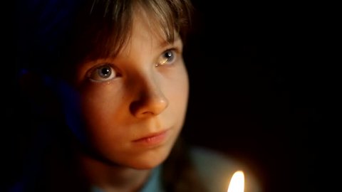 little Orthodox girl praying with a candle in her hand in a dark room