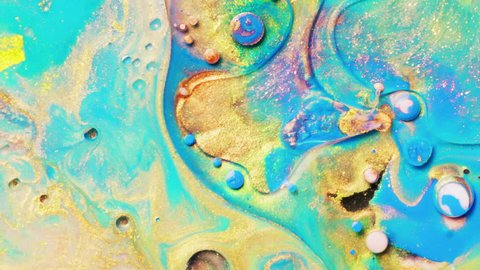 Colorful sparkling paints mix in beautiful patterns. Oil ink of yellow, blue and other colors spread on the surface and mix one into another creating amazing textures and design.