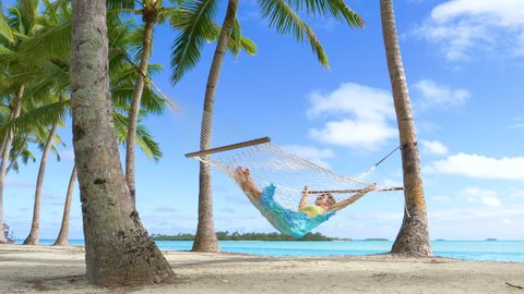LOW ANGLE: Sleeping Caucasian woman sways in a rope hammock on the spectacular tropical white sand beach in Cook Islands. Relaxed female tourist enjoying her summer vacation by taking a nap by ocean.