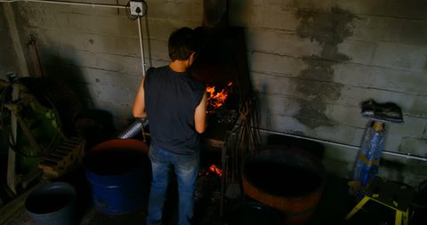 Rear high angle view of an attentive young female metalsmith with short hair heating horseshoe in fire.