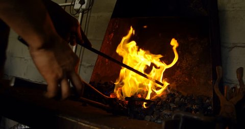 Close-up of young female metalsmith hands and tool heating horseshoe in fire.Close-up of young female metalsmith hands and tool heating horseshoe in fire.