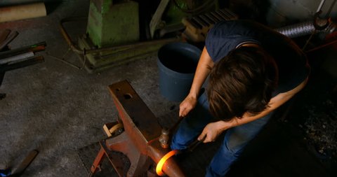 Overhead of young female metalsmith with short hair molding horseshoe in factory.
