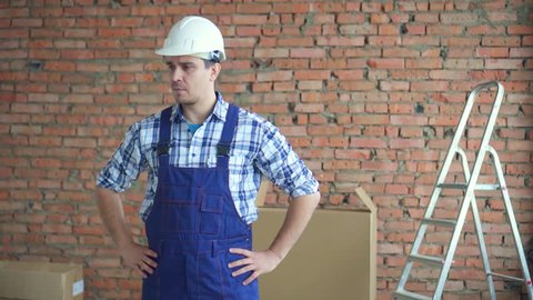 Puzzled man in a working uniform and white helmet against a brick wall