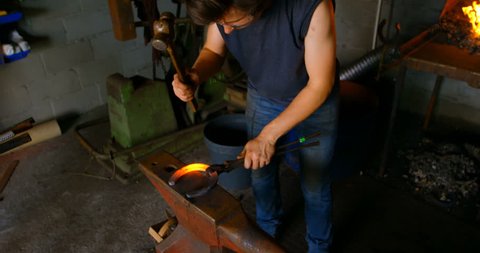 High angle view of young female metalsmith with short hair molding glowing hot horseshoe in factory 4k
