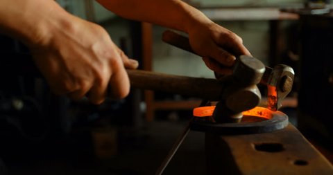 Close-up of female metalsmith hands and tools molding glowing hot horseshoe in factory. Hitting it with a chisel and a hammer.