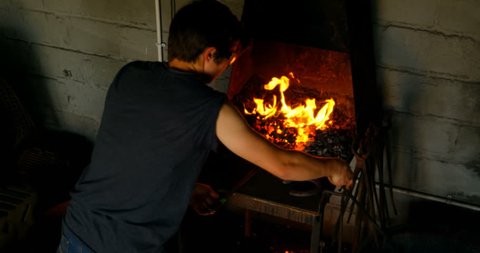 Rear view of a young female metal smith with short hair heating horseshoe in fire 