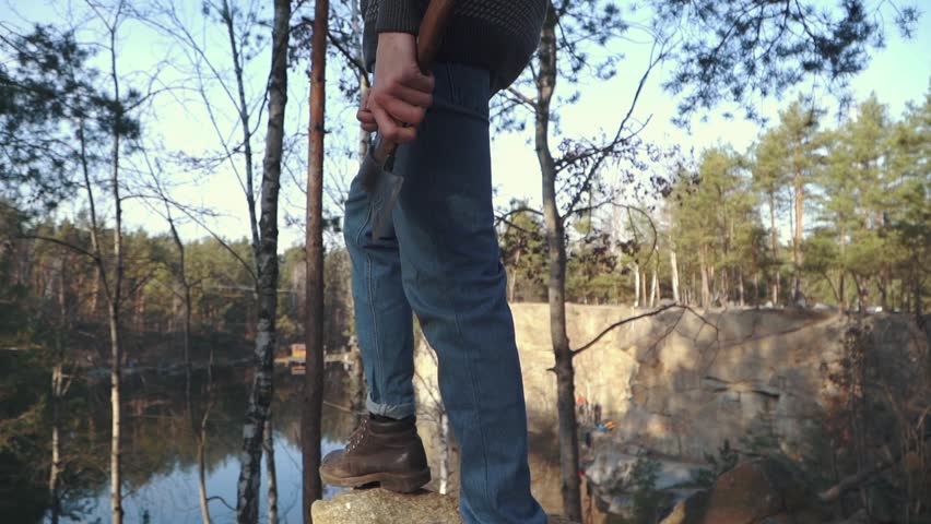 Male stand on the hill with ax. A man with an ax standing on a cliff.