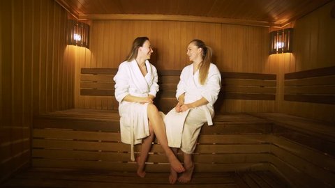 Two happy women talking to each other in a sauna