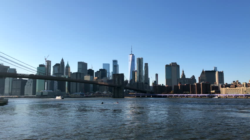 NEW YORK, USA - NOVEMBER 11, 2018: The skyscrapers in the financial district and the Brooklyn Bridge viewed from over the East River in the Dumbo neighbourhood of Brooklyn, New York, USA. | Shutterstock HD Video #1020857776