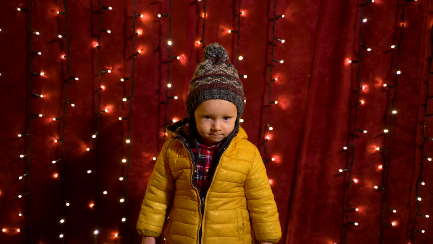 Young boy posing serious in front of lights wall at Christmas market.