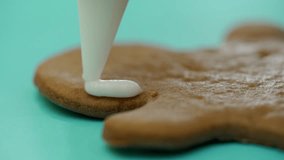 A confectioner is drawing a contour on ginger biscuits by white icing with using a confectionary nozzle for Christmas. Ginger man. Sweets. Close-up