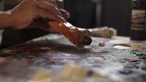 An Artist Squeezes Out Some blue Paint From A Tube Of Oil Paint on wood board.  slow motion close up shot artistic movement, making ready to paintbrush creative in studio. 