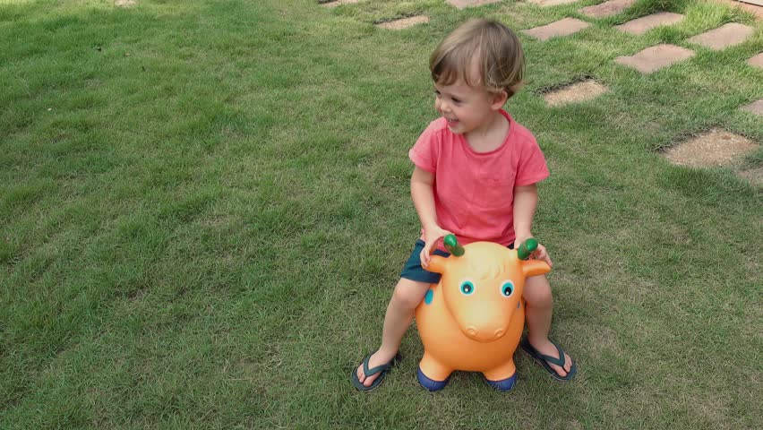 Little boy to ride on rubber toy cow on green meadow in yard