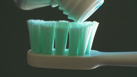 Squeezing toothpaste from tube onto toothbrush. Black Background