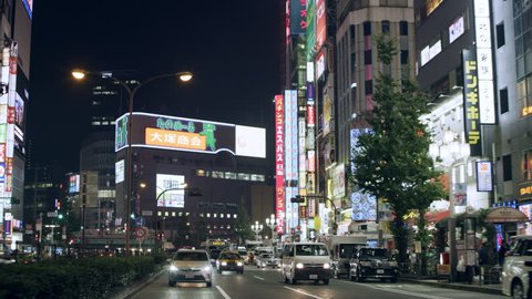 TOKYO, JAPAN - CIRCA October, 2018: Cars driving in a busy street past buildings with multiple advertisements at night. Wide shot on 4k RED camera