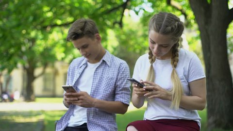 Gadget addicted friends using phones in park, lack of communication, ignoring