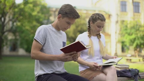 Two teenagers reading books in park, preparing for examination, studying