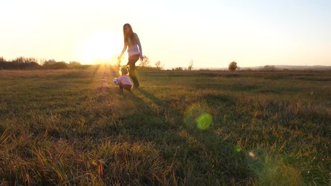 child plays ball on field, mother looks after daughter. kid throws hands of soccer ball on grass in park at sunset. Slow motion