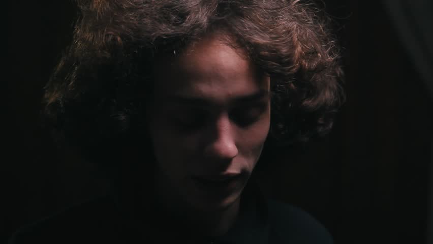 angry man with long hair talking on the phone in the dark room, close up
