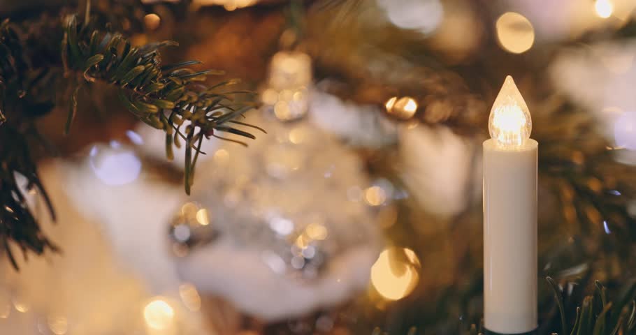 Festive White Ornaments and Twinkling Lights on a Christmas Tree. SLOW MOTION CLOSE UP. Happy preparation for winter holidays, bulbs, toys and candles on a fir tree. Cozy atmosphere.
