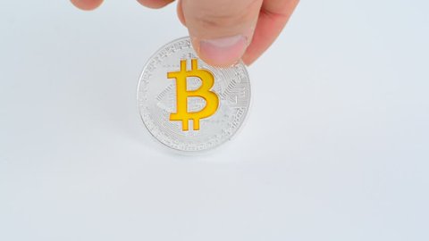 Putting down silver bitcoin coin with golden letter B on white backround.