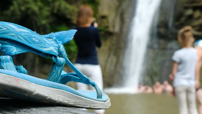 Close-up of sandals stand against the background of people bathing under a waterfall in defocus