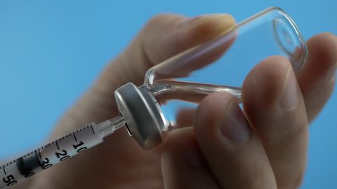Health worker dials the vaccine into a syringe on blue background. Russia coronavirus vaccine, Sputnik V. Covid-19 vaccination concept