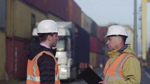 Port manager and a colleague tracking inventory while standing together by freight containers on a large commercial shipping dock