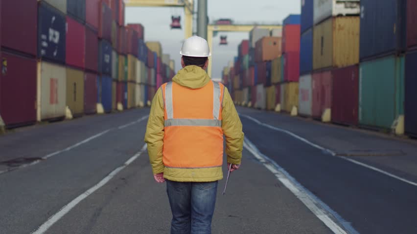 Engenier in white helmet and uniform walking through shipping dock for checking. Royalty-Free Stock Footage #1020927865