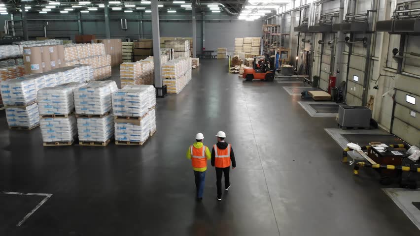 Rear view of warehouse team discussing while walking in warehouse. Aerial, top view. Royalty-Free Stock Footage #1020927880