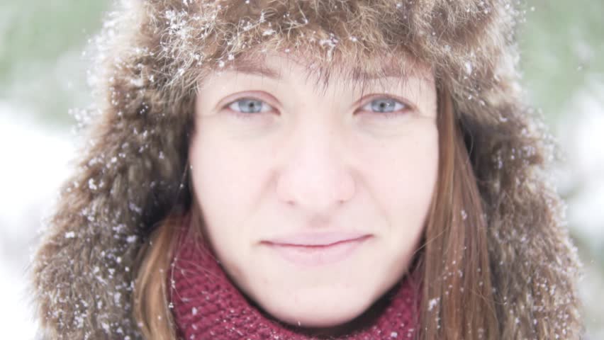 Young beautiful woman on a walk in the park in winter. Close-up of her face, snow flies into her face. She is happy, she is getting away. A large fur hat covers the ears on her head.