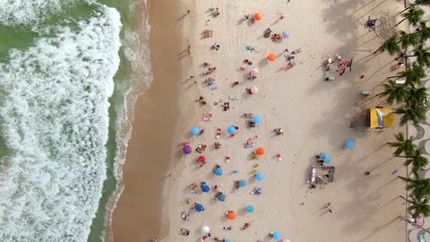 Copacabana beach in Rio de Janeiro, Brazil, top aerial view of waves crashing on the beach with people and umbrellas on the shore on a beautiful summer day.