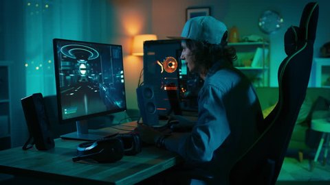 Professional Gamer Playing First-Person Shooter Online Video Game on His Powerful Personal Computer. Room and PC have Colorful Neon Led Lights. Young Man is Wearing a Cap. Cozy Evening at Home.