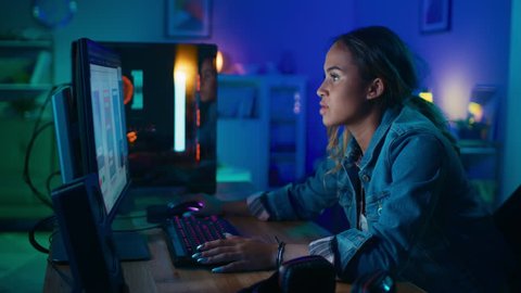 Beautiful Black Girl Freelance Designer Works with Mobile Interface Designs on a Powerful Gaming Computer at Home. She's Concentrated and Zooms In Her Art. Cozy Room is Lit with Warm and Neon Light.