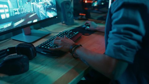 Close Up Hands Shot Showing a Gamer Pushing the Keyboard Buttons while Playing an Online Shooter Video Game. Keyboard Led Lights Change Color in Rainbow Spectrum. Gamer is Wearing a Bracelet.