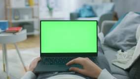 Woman at Home Lying on a Couch using Laptop Computer with Green Mock-up Screen. Girl Using Computer, Internet, Social Networks Browsing. Point of View Camera Shot.