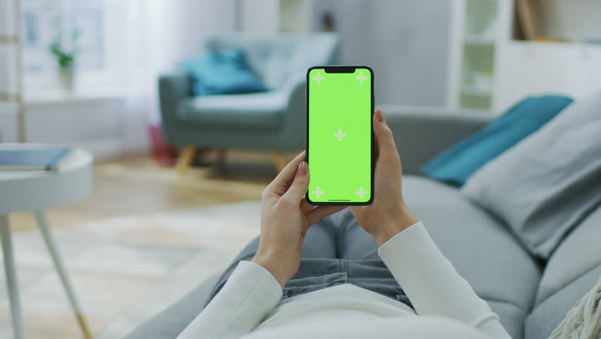 Young Woman at Home Uses Green Mock-up Screen Smartphone. She's Sitting On a Couch in His Cozy Living Room. Point of View Camera Shot. | Shutterstock HD Video #1020934222
