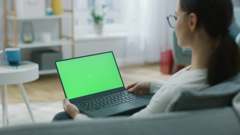 Young Woman at Home Sitting on a Couch Works on a Laptop Computer with Green Mock-up Screen. Girl Using Computer, Browsing through Internet, Watching Content, Chatting in Social Networks with Friends. 스톡 비디오