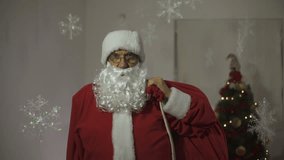 Santa Claus with fingers countdown to the new year, man with costume and gift bag waving hand and sending kiss to the camera, funny video, decorated snowflakes and Christmas tree in background of room
