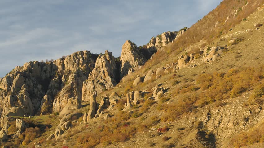 Aerial for a beautiful mountain in the sunny evening on a blue sky background. Shot. Steep rocks in profile in autumn sunny evening on cloudy blue sky background.