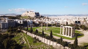 Aerial drone video of iconic pillars of Temple of Olympian Zeus and world famous Acropolis hill with masterpiece Parthenon on top at the background, Athens historic center, Attica, Greece