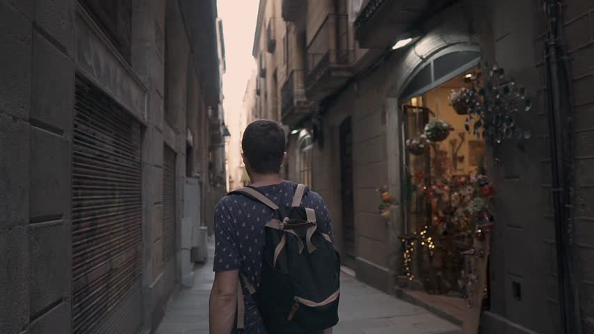 Adult man is walking in city lane in downtown, looking on old houses. He is stopping near small cozy gift store and watching it