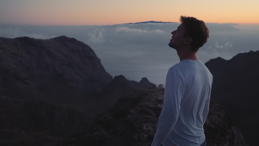 the man thoughtfully looks in the sky on the edge of the earth on top of the mountains above the clouds Royalty-Free Stock Footage #1020956974