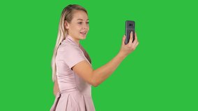 Female in pink dress making video call with her smart phone on a Green Screen, Chroma Key.